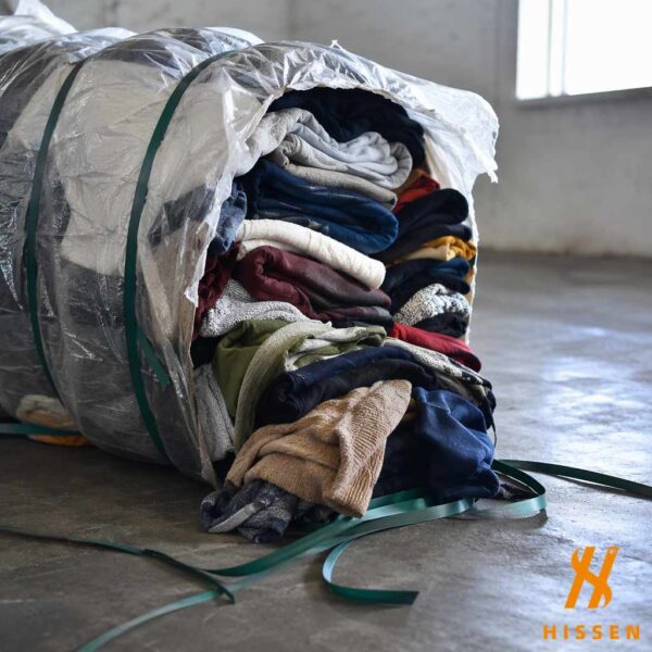 A compressed bale of used clothing partially opened with garments spilling onto a warehouse floor