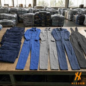 Second hand coveralls, navy work trousers and a bib overall arranged in rows on a warehouse sorting table