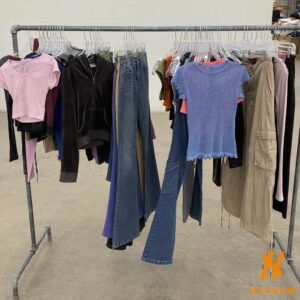A clothing rail hung with early 2000s garments including cropped baby tees, low-rise bootcut denim, a velour hoodie, cargo trousers and a mesh top
