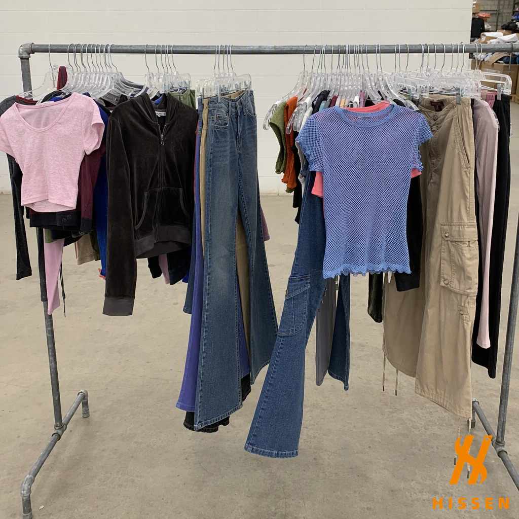 A clothing rail hung with early 2000s garments including cropped baby tees, low-rise bootcut denim, a velour hoodie, cargo trousers and a mesh top